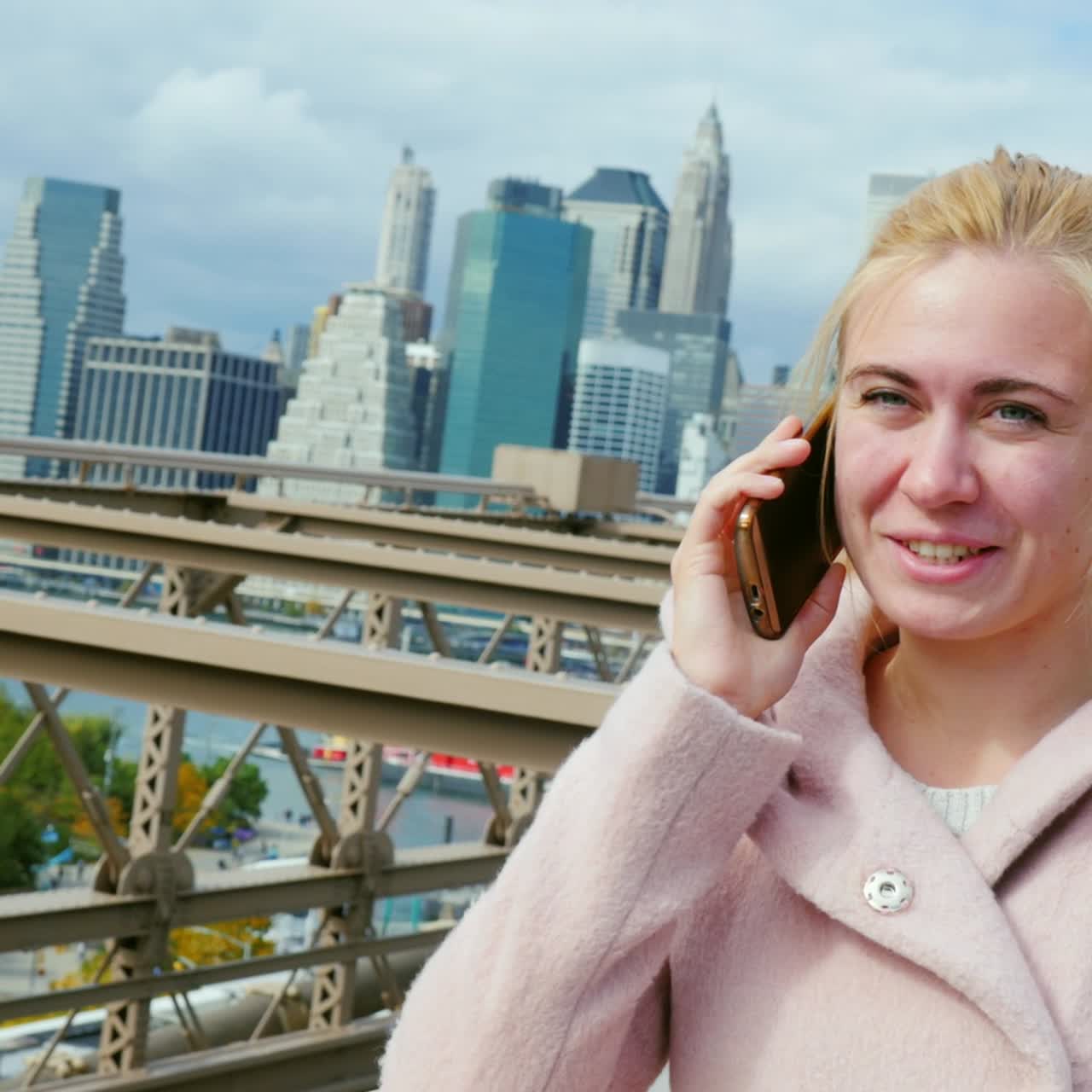 한 젊은 여성이 뉴욕 브루클린 다리에 서서 전화를 받고 있다