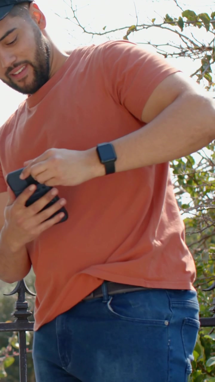 Vertical video: Bending by wheel, man in rust T lifting bag in front yard, offering, checking phone