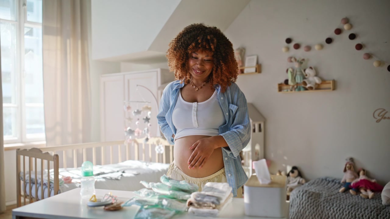 Expectant mother arranging diapers nursery table. Pregnant woman stroking belly.