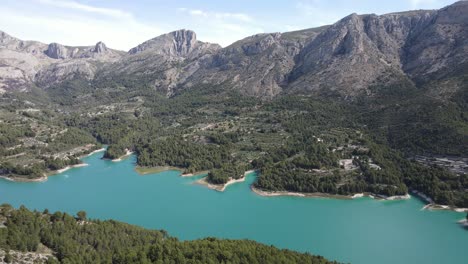 Dramatisch-Blauer-Türkisfarbener-See,-Umgeben-Von-Bergigem-Gelände-Und-Wald,-Sonnig