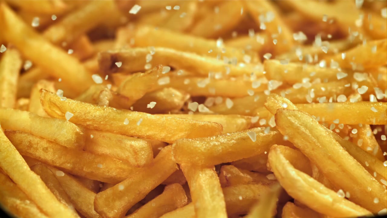 Close-up em Câmera Lenta de Sal Caindo sobre Batatas Fritas Douradas