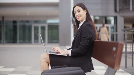 Frau-Schaut-Mit-Laptop-Auf-Bank-Herüber