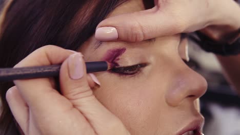 applying purple eyeliner in the outer corner and outer crease to create a flawless smokey eyes look. brunette caucasian looking girl with hazelnut eyes.