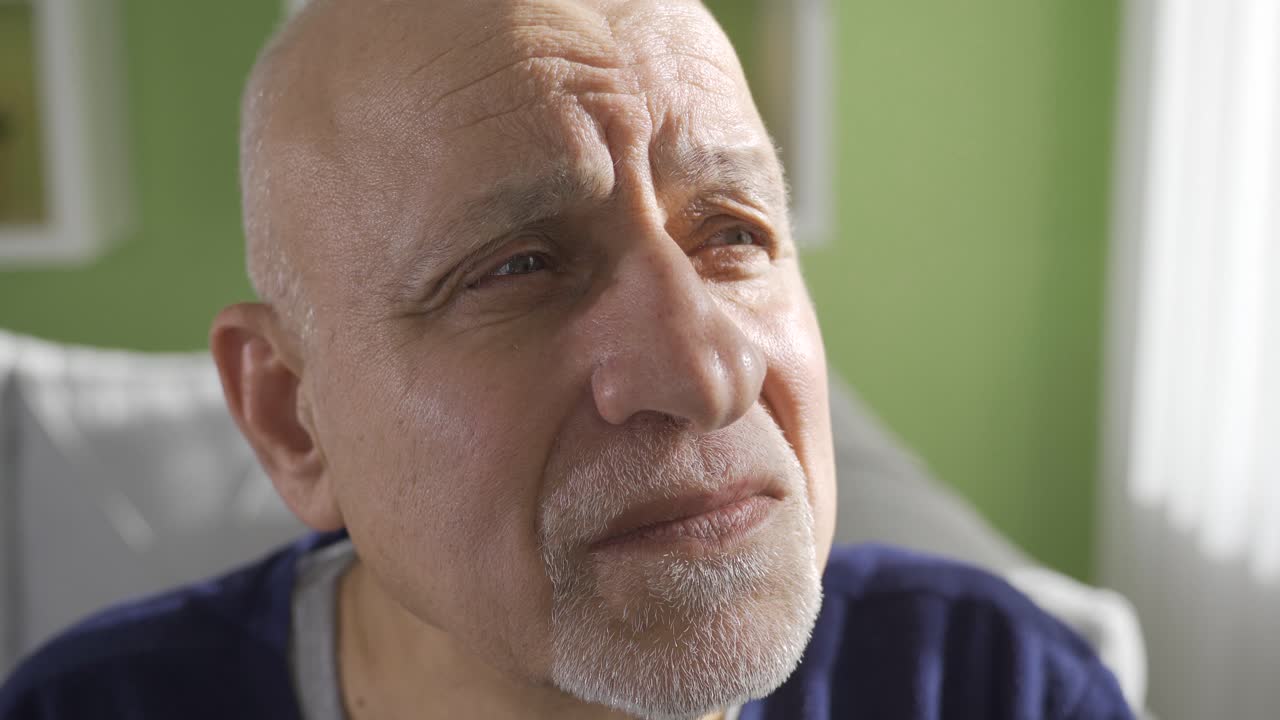 Close-up depressed old retired man sitting on sofa, feeling lonely and unhappy.