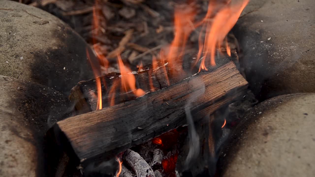 Chopped wood burning on hot smoking campfire outdoors in the forest.Close up zooming out.