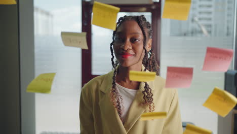 smalling african american business woman using sticky notes brainstorming problem solving strategy on glass whiteboard leader woman showing solution for project deadline in office.