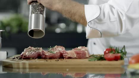 chef masculino pimienta la carne en la cocina. primer plano chef manos pimienta filete
