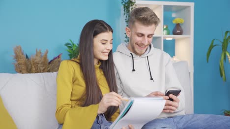 hombre joven y mujer joven sentados en el sofá en casa haciendo una lista.