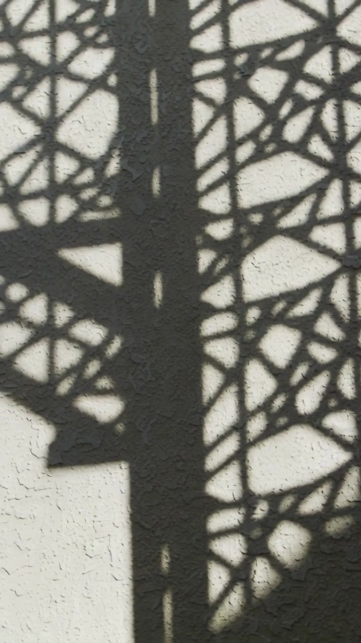 Video vertical: Sombra de celosía cambiante deslizándose por el estuco a medida que el sol se mueve, proyectando formas de poste y escalón