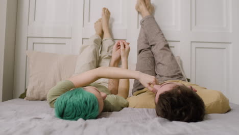 loving couple holding hands and looking at each other while lying on a cozy bed with their legs up on the wall