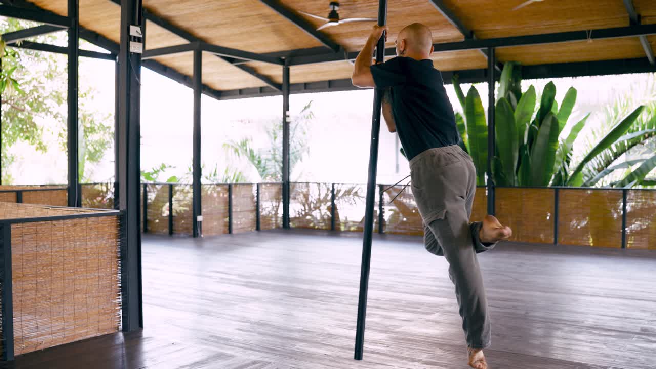 Skillful Man Performing Pole Balancing Act in Tropical Studio