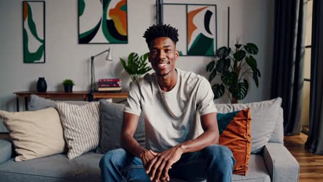casual home setting with a young man sitting on a sofa, smiling. side angle shot captures a relaxed