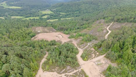 Aerial-orbital-view-of-barren-land-left-from-deforestation,-surrounded-by-remaining-forest,-Cornwall,-UK