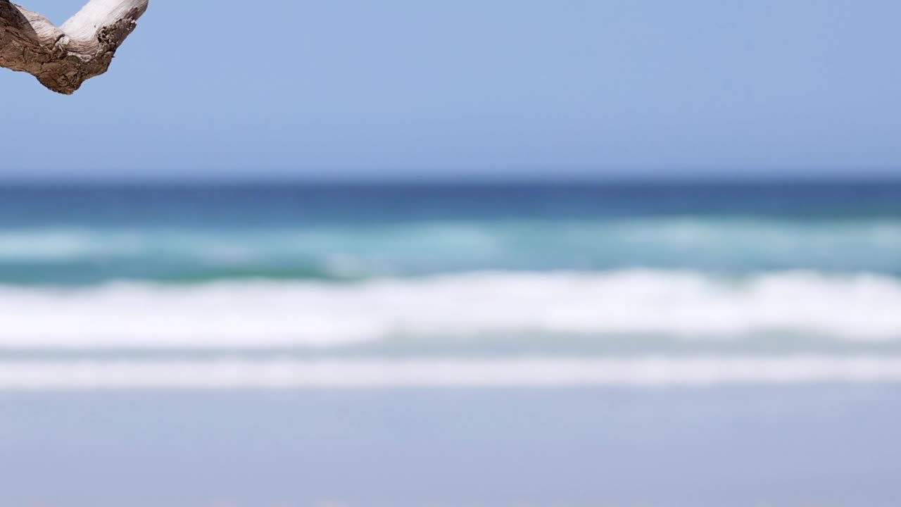 A serene view of ocean waves rolling onto a sandy shore under a clear blue sky.