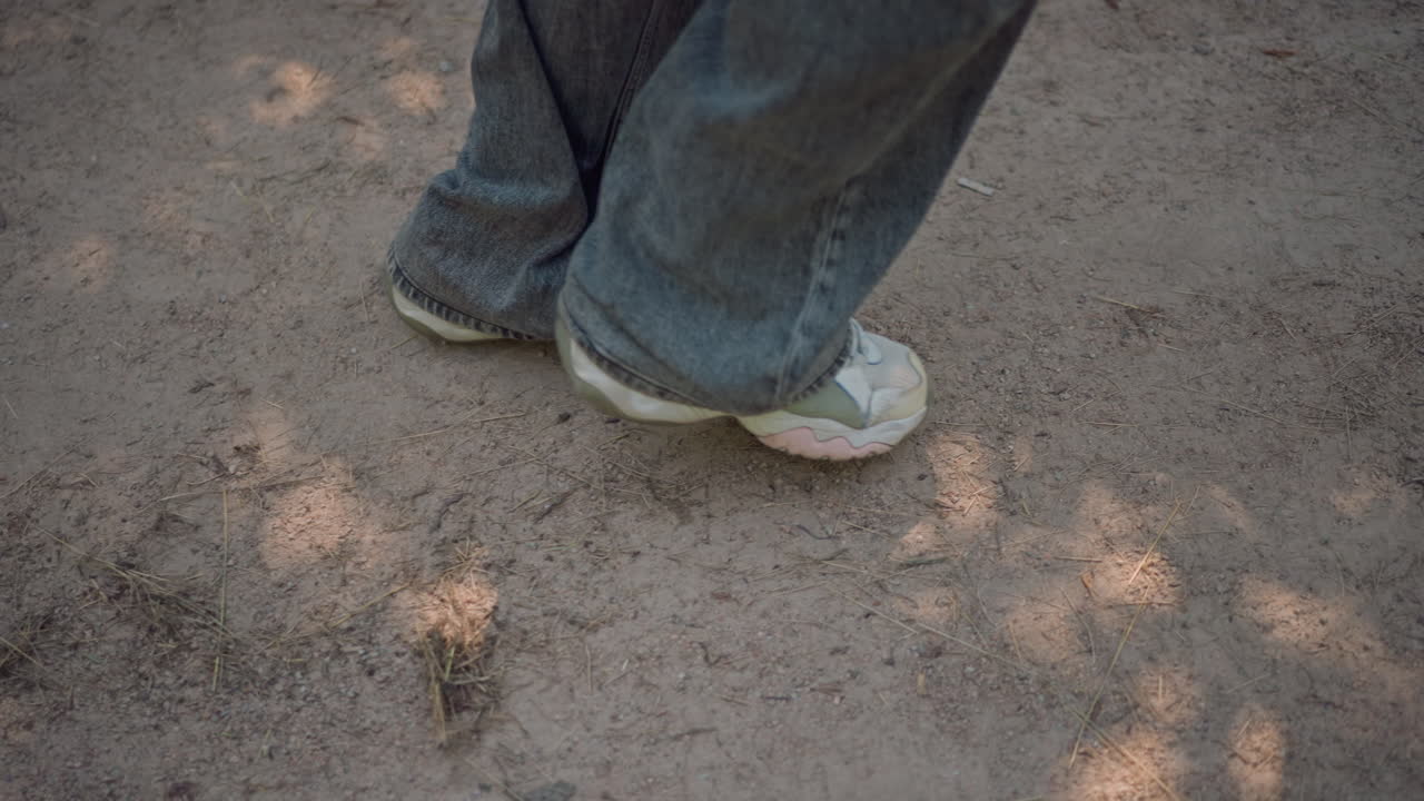Sneakers on dirt, Casual student walking outdoors, Student shoes strolling on earthy ground in warm sunlight, Casual student footwear moving slowly over soil beneath dappled sunlight shadows