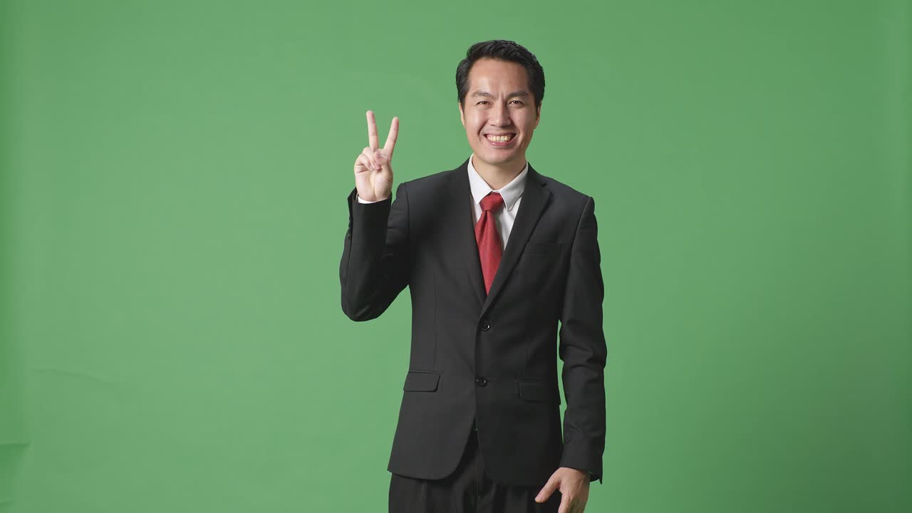 아시아 사업가 한 명 이 스튜디오 의 녹색 스크린 에 서 있는 동안 평화 로운 몸짓 과 미소 를 보이고 있다