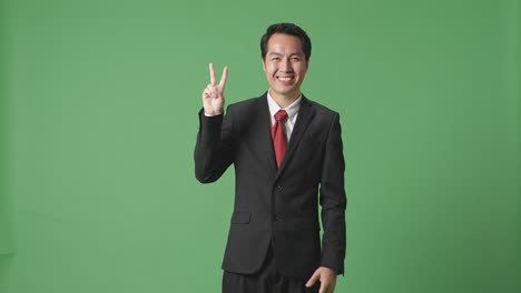 아시아 사업가 한 명 이 스튜디오 의 녹색 스크린 에 서 있는 동안 평화 로운 몸짓 과 미소 를 보이고 있다