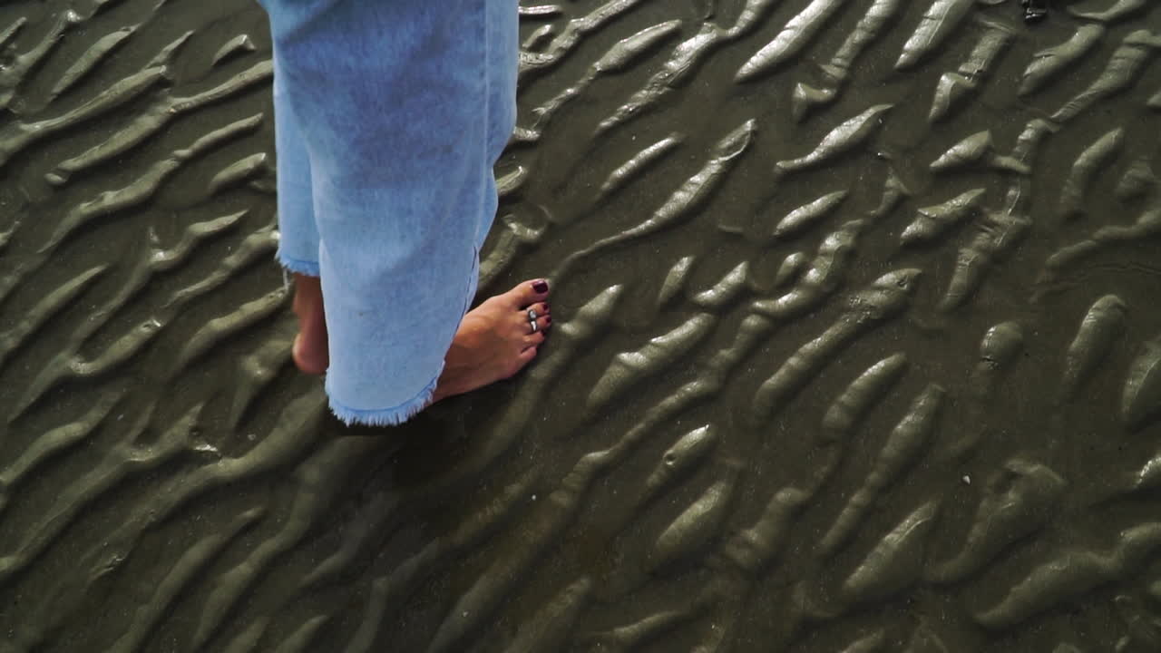 Donna a piedi nudi che cammina sulla sabbia bagnata della spiaggia