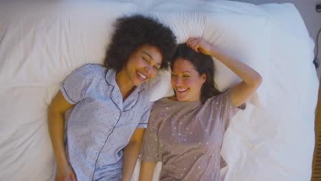 overhead portrait shot of loving same sex female couple wearing pyjamas lying on bed at home