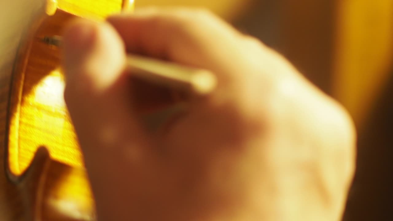 바이올린 제작자 루티에의 손이 손으로 만든 목조 현악기를 바르닝하고 있습니다.