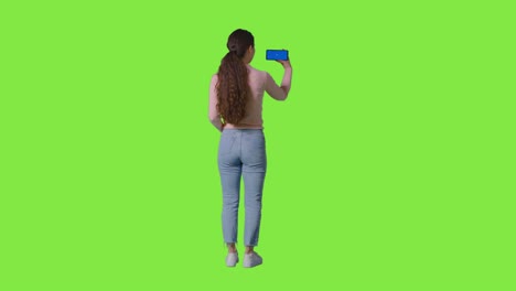 full length studio rear view of woman streaming on blue screen mobile phone against green screen