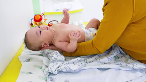 mother is taking baby and puts him on the clothes. baby in diaper is looking up. side view. blurred backdrop.