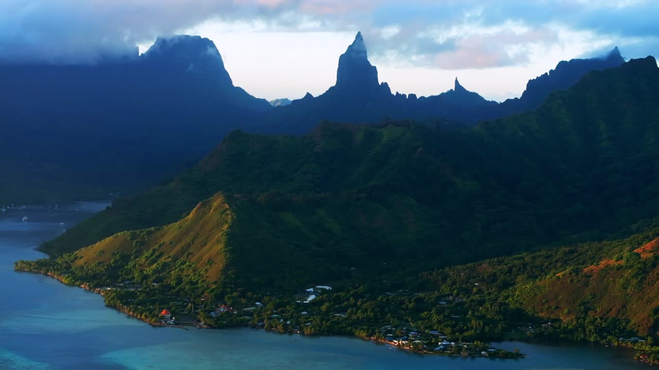 Golden hour sunset Cooks Opunohu Bay Moorea island French Polynesia aerial drone clouds covering Mount Mauaroa Tohivea Rotui clouds lagoon coral reef waves Pacific Ocean circle left parallax