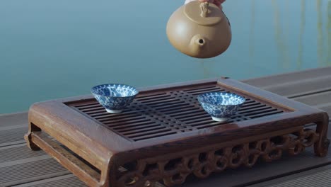 beautiful chinese tea ceremony near water slow motion eastern culture style. female hand pouring fresh steaming drink into cups. meditative calm mood and atmosphere