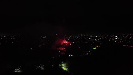 Toma-Aérea-De-Pequeños-Fuegos-Artificiales-Rojos-De-Múltiples-Disparos-Explotando-Por-La-Noche