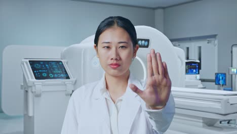 close up of asian woman doctor making stop gesture while standing with mri machine in the hospital