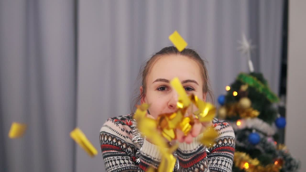 Close Up view of beautiful woman blowing gold glitter confetti at home in slow motion. Beautiful young party woman blowing gold