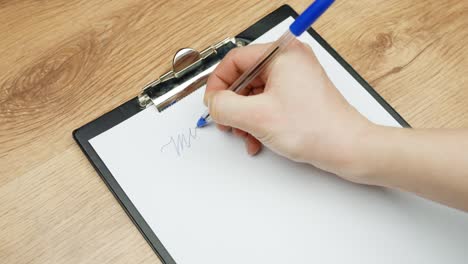 close up of a hand writing “my business” with a blue pen on white paper clipped to a clipboard, startup concept