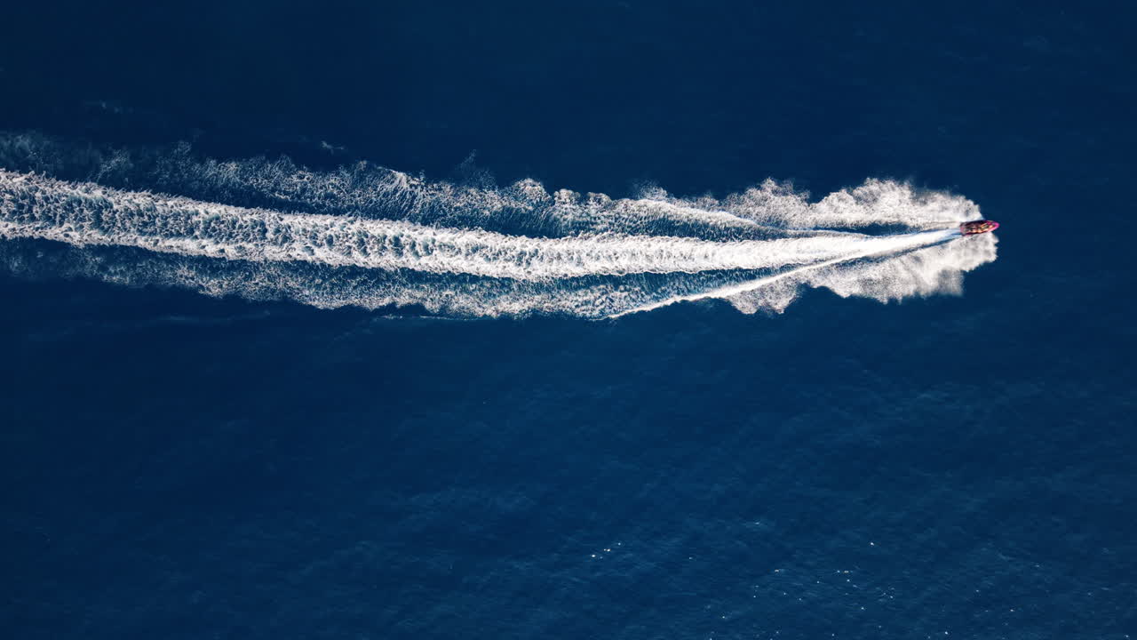 Motoscafo solca l'oceano blu, vista aerea, lasciando una scia bianca.