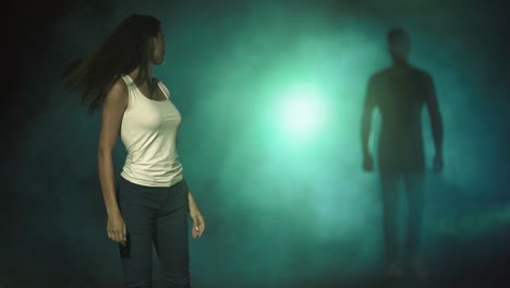 the woman walking in a dark street against a man in a smoke behind. slow motion