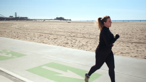 determined young woman jogging on the pathway of the sandy beach of santa monica california