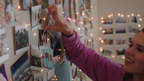 happy teenage girl sticking photos on wall in bedroom making collage enjoying hanging out with friends on weekend sharing photograph collection