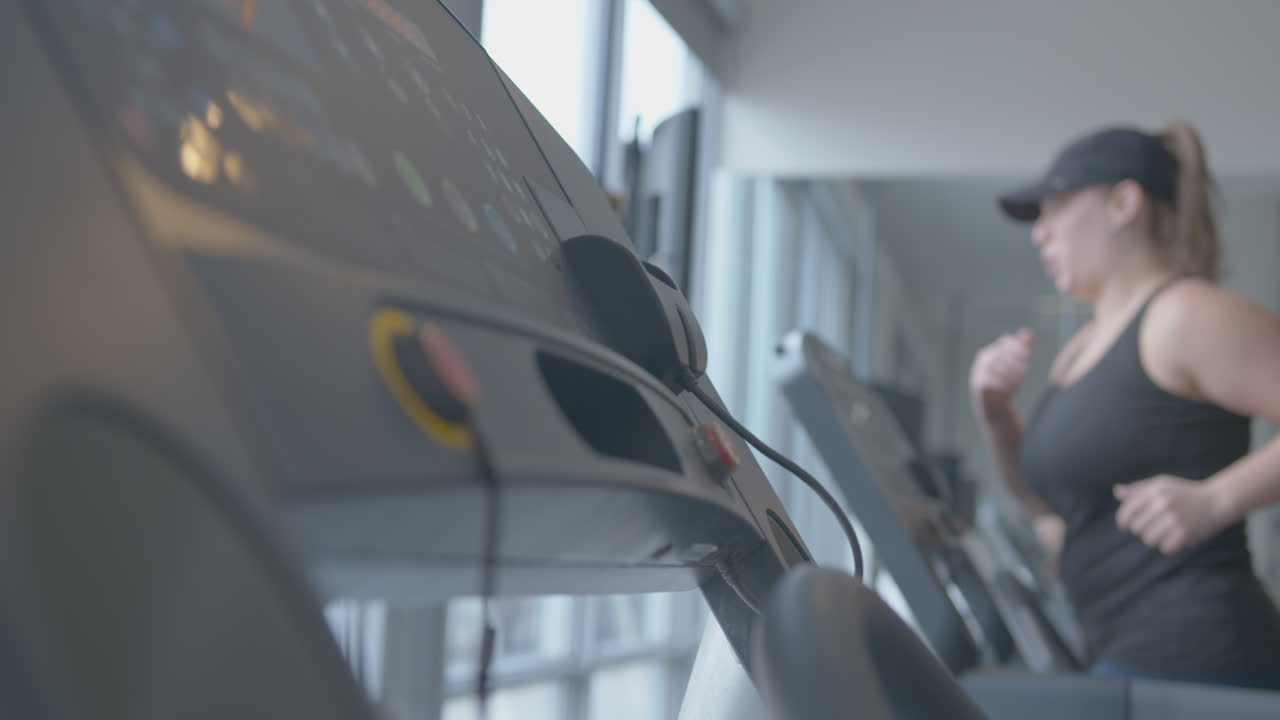 Wide Rack Focus Pan of a Woman Jogging on a Treadmill