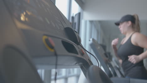 wide rack focus pan of a woman jogging on a treadmill