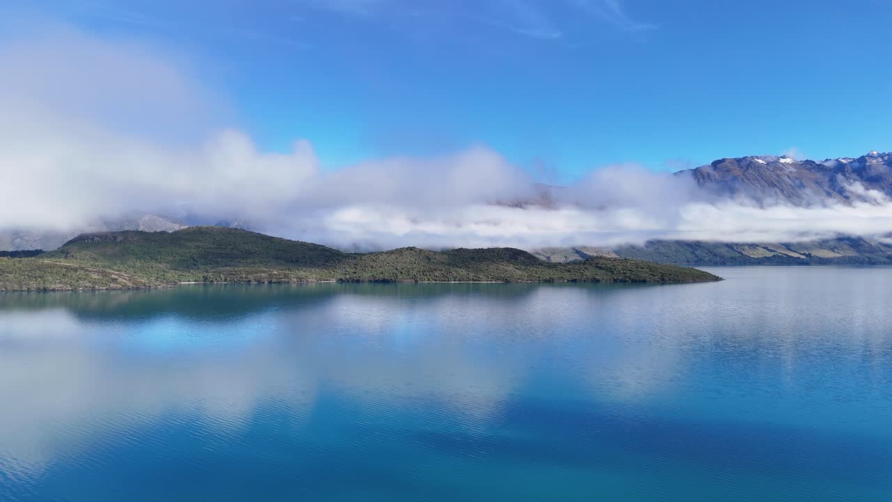 Drone footage captures serene views of Lake Wakatipu and surrounding mountains under clear blue skies in Glenorchy, New Zealand