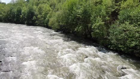 drone view in albania flying over a moving rapids river between green mountains on a sunny day