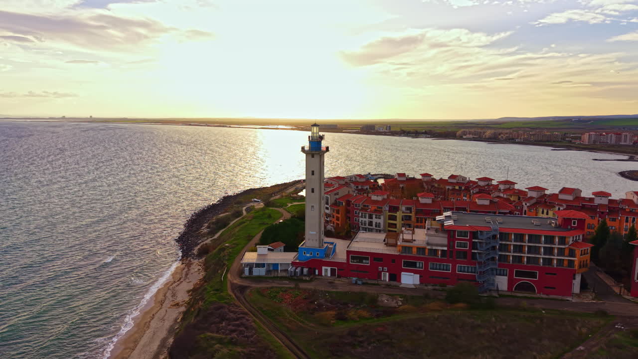 Vista del tramonto di un faro costiero ed edifici colorati in riva al mare in un paesaggio sereno