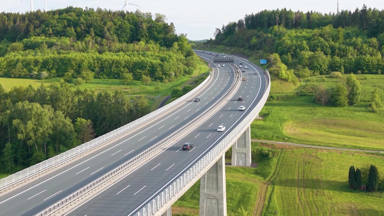 Vue aérienne par drone du pont de l'autoroute A9 en Bavière avec un trafic en mouvement traversant une campagne verdoyante, mettant en valeur l'infrastructure de transport moderne en Allemagne, UHD.