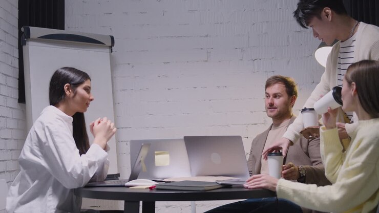 Young Man Bringing Takeaway Coffee To His Happy Colleagues During A Team Meeting 1