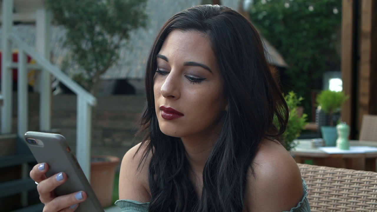 joven morena segura y atractiva con un top informal, usa su teléfono celular, sonríe alegremente a los mensajes de texto, mira a su alrededor con ropa elegante, chica milenaria