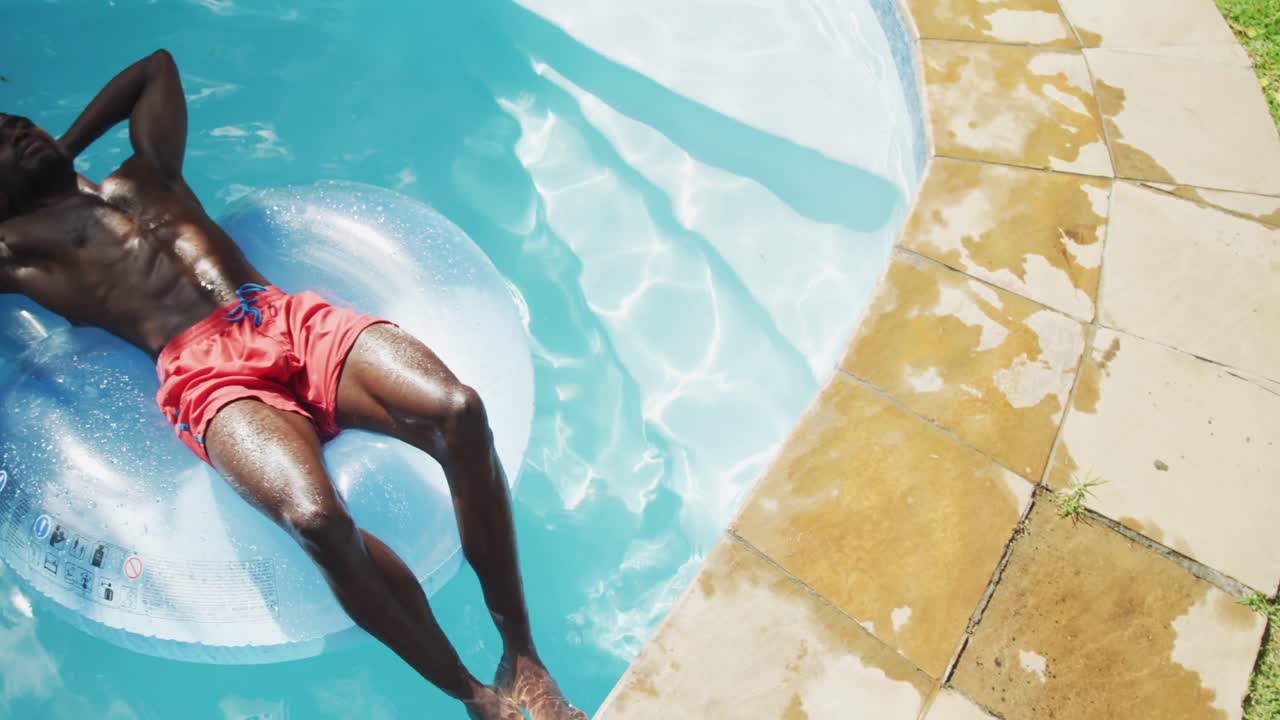 Handsome african american man lying on inflatable sunbathing in swimming pool
