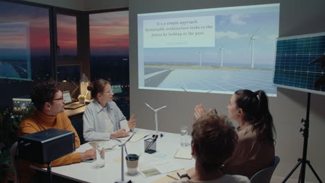 team of engineers discussing presentation about energy efficient architecture during business meeting in the office. high angle shot, scenic sunset over cityscape behind the windows