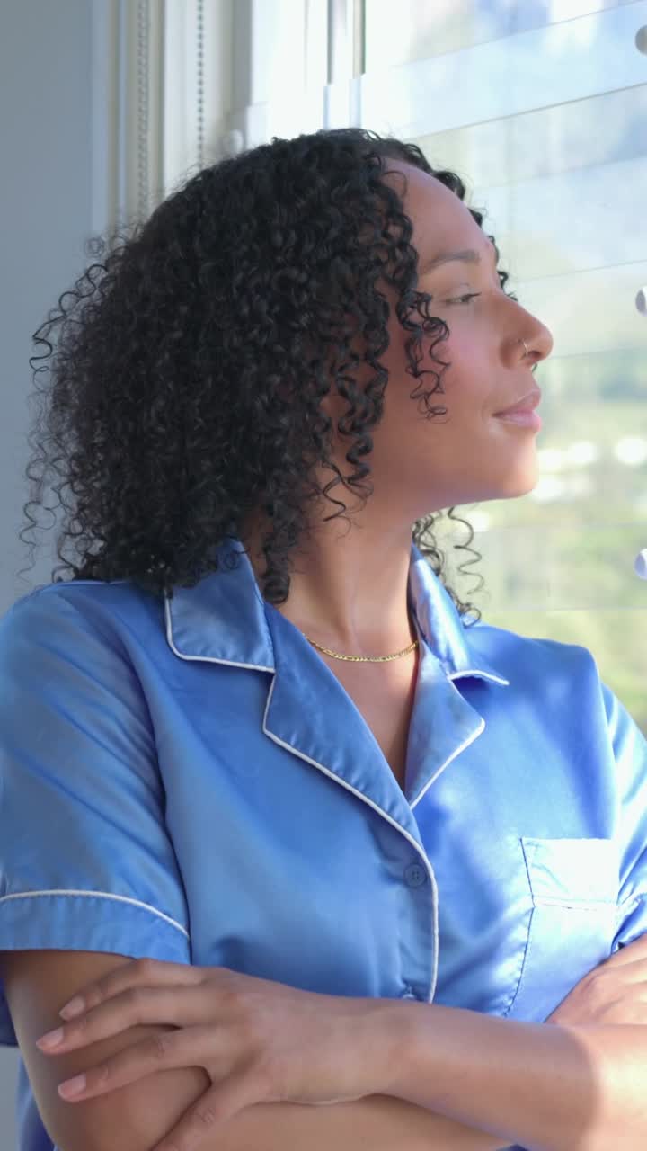 Vertical video: Reacting to sun through window, woman in blue satin top turning head, closing eyes