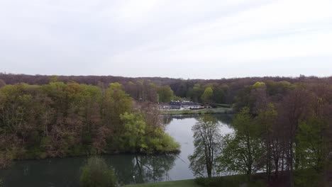 Tiro-De-Drone-De-Una-Casa-Del-Lago-En-Un-Parque-En-El-Cinturón-Verde-De-Colonia-En-Alemania