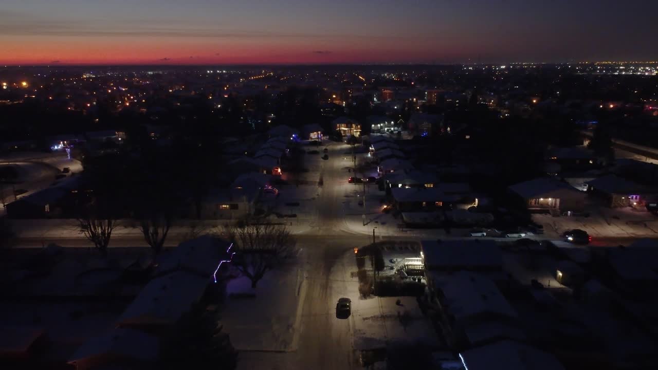 Snowy street at dusk, surrounded by illuminated houses in the residential neighborhood of St Constant, Quebec. Dolly Back, Rising Shot