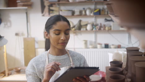 Female-Potter-In-Ceramics-Studio-Carrying-Out-Inventory-Using-Digital-Tablet